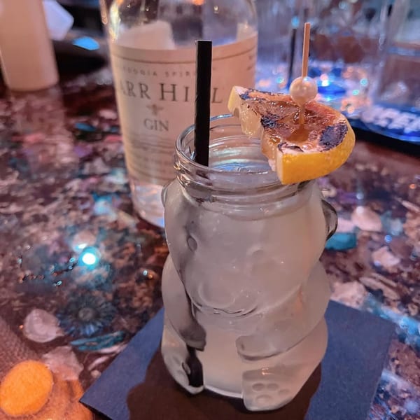 A Celona Gin Lounge cocktail in a bear-shaped glass, garnished with a charred orange slice.