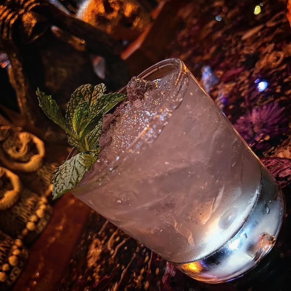 A refreshing Celona Gin Lounge cocktail with crushed ice and mint garnish, on a dark, textured surface.